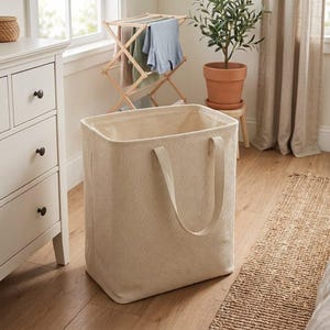 May include: A rectangular laundry hamper made of beige fabric with a textured weave. The hamper features two matching fabric handles attached to the upper sides, a wide open top, and a structured, upright design for holding clothing or household items.