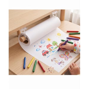 Op de afbeelding: Een witte papierrol gemonteerd onder een houten tafel met doorzichtige plastic beugels, met een kleurrijke kindertekening van een huis, auto, zon en vlinders. Verschillende waskrijtjes in blauw, geel, groen en rood liggen op de tafel.