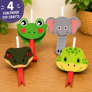 Könnte beinhalten: Vier Papierspielzeuge mit Tiergesichtern: ein grüner Frosch mit roten Herzen, ein grauer Elefant, eine dunkelgrüne Schlange mit roten Augen und eine hellgrüne Schlange. Jedes Spielzeug hat einen weißen Strohhalm und eine rote Zunge aus Papier.