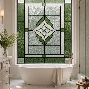 Op de afbeelding: Een rechthoekig raam met een glas-in-loodontwerp met een centraal ruitmotief, groene getextureerde glaspanelen en heldere glazen secties met patronen in een zwart metalen frame, geplaatst boven een wit ovaal vrijstaand bad.