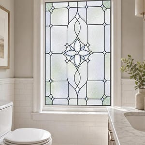 May include: A rectangular window featuring a decorative leaded glass design with a central floral motif. The glass panels are textured and translucent, framed by thin black metal lines that create a geometric pattern of squares and curves.
