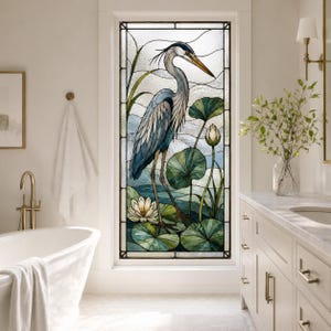 Könnte beinhalten: Ein rechteckiges Buntglasfenster mit einer detaillierten Darstellung eines Blaureihers, der zwischen grünen Seerosenblättern und weißen Seerosen steht. Das Design verwendet verschiedene Glasstrukturen für Wasser und Himmel, eingefasst in dunkles Metall.