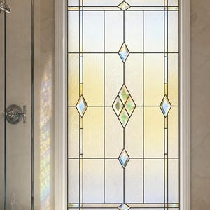 Puede incluir: Una ventana rectangular con marco blanco que presenta vidrio emplomado decorativo. El vidrio tiene un acabado texturizado y translúcido con un patrón geométrico de líneas verticales y varios detalles en forma de diamante en una columna central.