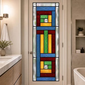 Könnte beinhalten: Eine weiße Innentür mit einem hohen, rechteckigen Buntglaseinsatz. Die Glasscheibe zeigt ein geometrisches Muster aus blauem, rotem, grünem und gelbem strukturiertem Glas, akzentuiert durch kleine, klare, quadratische Glaselemente.