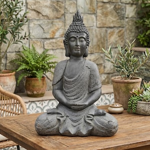 Può includere: Una statua di Buddha grigio scuro in posizione seduta meditativa con le mani appoggiate in grembo. La figura presenta una veste testurizzata, un'espressione facciale serena con gli occhi chiusi e un ushnisha appuntito sulla testa, finitura pietra.