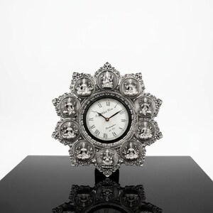 Può includere: Un orologio da parete color argento con quadrante circolare con numeri romani e la scritta "Royal Clock Works" e "Birmingham est 1997". La cornice a forma di stella presenta dieci rilievi circolari che raffigurano varie divinità.