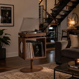 May include: A walnut wood record player stand featuring a rectangular storage compartment with a circular side cutout, a central support column, and an oval base. The stand holds a turntable with a clear dust cover and a collection of vinyl records.