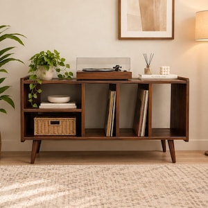 Può includere: Una console multimediale in legno scuro con gambe affusolate e diversi scomparti aperti. La superficie superiore ospita un giradischi, mentre i ripiani contengono una pianta, una ciotola bianca, un cestino e dei dischi in vinile.