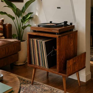 May include: A dark wood record player stand with four tapered legs, featuring an open storage compartment filled with vinyl records and a side rack. An Audio-Technica turntable with a clear dust cover sits on the top surface of the unit.