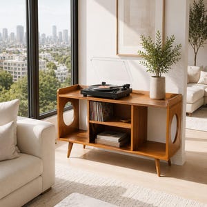 May include: A wooden media console with tapered legs and circular side cutouts. The top surface holds a black record player with a clear dust cover. The interior shelves contain a collection of vinyl records and stacked books.