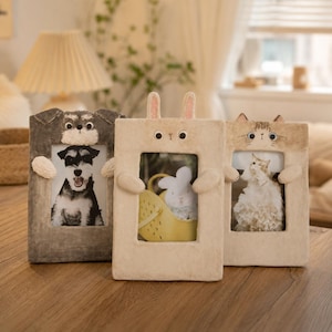 May include: Three rectangular photo frames featuring sculpted animal designs. The left frame is dark gray with a dog face, the center frame is cream with rabbit ears, and the right frame is light brown with a cat face. Each frame has small arms.