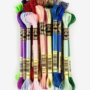 May include: A collection of 15 DMC embroidery floss spools in various colors, including green, blue, red, pink, and silver. The spools are labeled with DMC numbers and the words "Mouliné" and "DMC".
