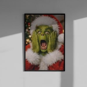Könnte beinhalten: Ein gerahmter Kunstdruck, der eine grüne Figur mit weit aufgerissenen Augen und offenem Mund zeigt, die Hände an die Wangen gepresst. Die Figur trägt ein rotes Weihnachtsmannkostüm mit weißem Kunstfellbesatz. Im Hintergrund sind Lichter zu sehen.