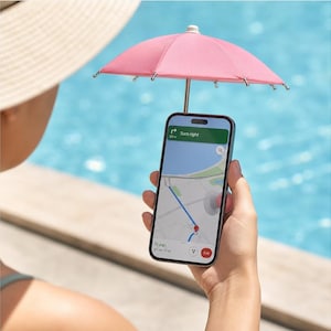 Op de afbeelding: Een smartphone met een navigatiekaart en een afslaginstructie, voorzien van een klein roze parasolletje aan de bovenkant van het toestel om het scherm buiten bij een blauw zwembad tegen de zon te beschermen.