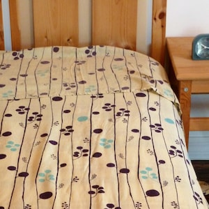 Puede incluir: Un edred&oacute;n estampado en amarillo y marr&oacute;n con un dise&ntilde;o sencillo de l&iacute;neas verticales y peque&ntilde;os c&iacute;rculos. El edred&oacute;n est&aacute; sobre un marco de cama de madera.