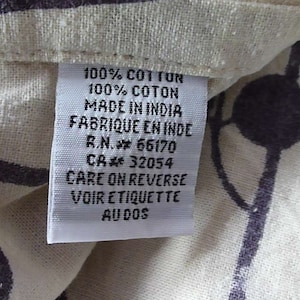 Puede incluir: Una etiqueta de tela de algod&oacute;n blanco con texto negro que dice "100% COT TUN 100% COTON MADE IN INDIA FABRIQUE EN INDE R.N. 66170 CA 32054 CARE ON REVERSE VOIR ETIQUETTE AUDOS".