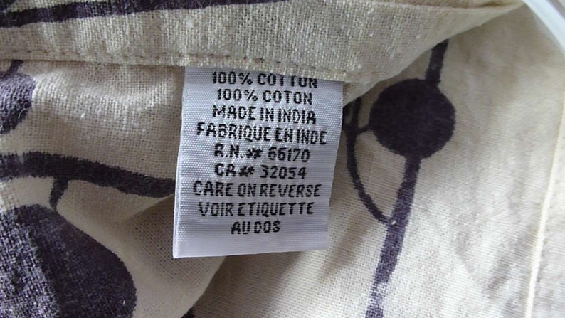 Puede incluir: Una etiqueta de tela de algod&oacute;n blanco con texto negro que dice "100% COT TUN 100% COTON MADE IN INDIA FABRIQUE EN INDE R.N. 66170 CA 32054 CARE ON REVERSE VOIR ETIQUETTE AUDOS".
