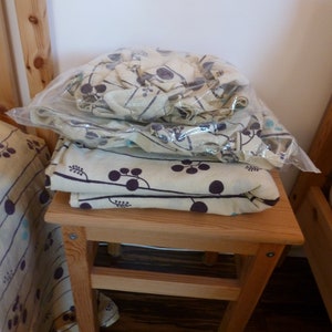 Puede incluir: Un taburete de madera con una tela estampada en blanco y marr&oacute;n en la parte superior. La tela tiene un dise&ntilde;o floral con peque&ntilde;os puntos negros.