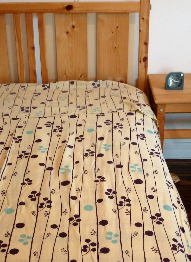 Puede incluir: Un edred&oacute;n estampado en amarillo y marr&oacute;n con un dise&ntilde;o sencillo de l&iacute;neas verticales y peque&ntilde;os c&iacute;rculos. El edred&oacute;n est&aacute; sobre un marco de cama de madera.