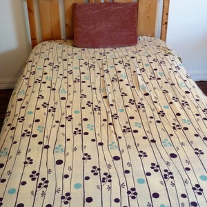 Puede incluir: Un marco de cama de madera con una cabecera y un piecero de color marr&oacute;n claro. La cama est&aacute; hecha con una colcha estampada en blanco y azul con una almohada marr&oacute;n oscuro en la parte superior.