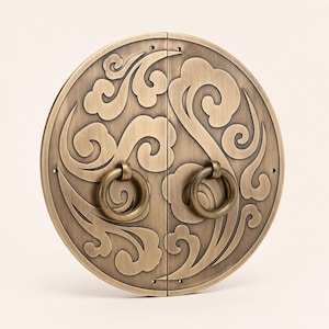 May include: A circular brass door plate featuring a split design with an embossed cloud pattern and two centered ring pulls. The metal has a brushed finish with dark recessed areas highlighting the intricate swirling motifs across the surface.