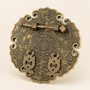 May include: A circular brass cabinet plate featuring an intricate embossed pattern of stylized bats and clouds. The hardware includes a horizontal sliding bolt mechanism and two ornate drop handles, with a central circular medallion design.