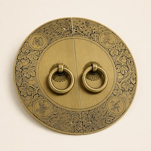May include: A circular brass door plate featuring two swinging ring handles. The plate is decorated with intricate engraved patterns of vines, leaves, birds, and four distinct Chinese characters enclosed in circular frames on the outer border.