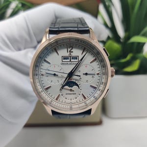 May include: A rose gold Jaeger-LeCoultre automatic wristwatch with a white dial, black leather strap, and moon phase display. The dial features a calendar showing 2027 and FEB, a pulsometer scale, and the text JAEGER-LECOULTRE and AUTOMATIQUE.