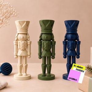 Könnte beinhalten: Drei stehende Nussknacker-Figuren in Creme, Olivgrün und Marineblau. Jede hat ein geometrisches, facettiertes Design mit hohem Hut, Uniformjacke und rundem Sockel. Ein kleines quadratisches Schild zeigt den Text in vielen FARBEN erhältlich.