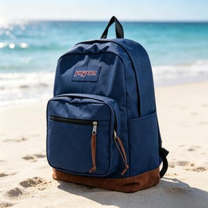 May include: A navy blue backpack with a brown suede bottom panel, featuring a top handle, adjustable shoulder straps, and a front zippered pocket with brown leather zipper pulls. The JanSport brand logo is stitched on the upper front section.