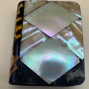 May include: A rectangular case featuring a side panel with a brown and black tortoiseshell pattern. The front surface is decorated with a geometric mosaic of iridescent mother-of-pearl tiles arranged in diamond shapes, set against a dark base.