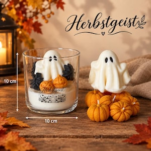 Könnte beinhalten: Ein durchsichtiges Kerzenglas mit einer weißen geisterförmigen Wachsfigur, kleinen orangefarbenen Kürbissen und schwarzen sternförmigen Wachsstücken. Das Glas trägt den Schriftzug "Herbstgeist" und ein Kürbis-Motiv. Maße: 10 cm mal 10 cm.