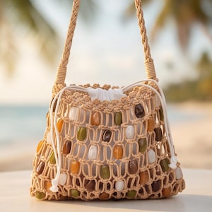 May include: A beige macrame drawstring bag featuring a woven net design embellished with smooth, multi-colored beads in shades of green, brown, and white. The bag includes a white fabric interior lining and a braided shoulder strap for carrying.