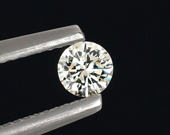May include: A clear round diamond gemstone held by silver tweezers against a black background.
