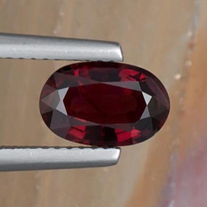 Peut inclure: Une pierre précieuse ovale rouge foncé tenue dans des pinces. La pierre précieuse est d'une couleur rouge foncé riche et a une surface lisse et polie.