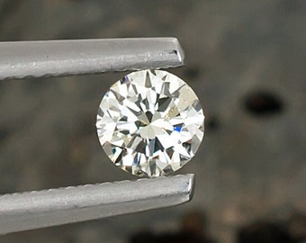 May include: A clear round diamond held by silver tweezers against a gray background.
