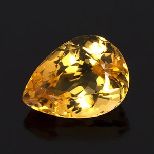 May include: A pear-shaped, faceted gemstone with a golden yellow color. The gemstone is set against a black background.