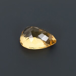 May include: A teardrop-shaped, faceted, golden yellow gemstone.