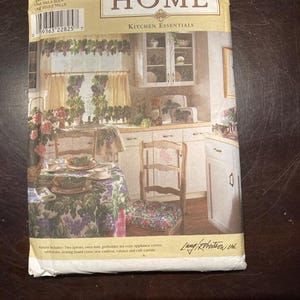 May include: A Simplicity Home Kitchen Essentials sewing pattern envelope, number 8690, featuring a printed illustration of a kitchen with a grape-themed tablecloth, seat cushion, valance, and cafe curtain. The text includes pattern contents.