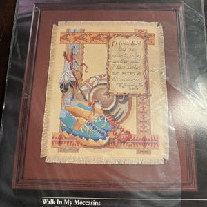 May include: A Bucilla counted cross stitch kit titled Walk In My Moccasins, featuring a design of blue moccasins, feathers, and a quote. The package includes 14 count Aida, cotton embroidery floss, a needle, and instructions, measuring 11.25 by 14.5 inches.