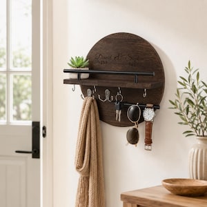 May include: A circular dark brown wooden wall-mounted organiser featuring a shelf with a black metal rail, five silver hooks, and the engraved text David & Sophia. The shelf holds a small potted succulent, while the hooks display a beige scarf, keys, sunglasses, and a wristwatch.