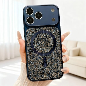 May include: A dark blue smartphone case featuring a textured back panel covered in small, shimmering gold and blue crystals. The case includes a circular magnetic ring in the center and a smooth, solid dark blue camera housing area at the top.