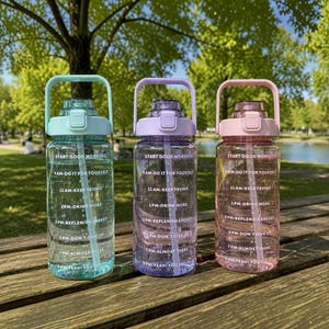 May include: Three translucent plastic water bottles in light blue, purple, and pink. Each bottle features a handle, a straw, and white printed text with hourly time markers and motivational phrases like Start Good Morning and Yeah! You Did It.