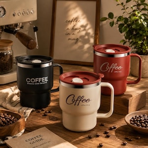 Könnte beinhalten: Drei Reisebecher aus Edelstahl mit Deckel und Henkel in Schwarz, Creme und Rot. Jeder Becher trägt das Wort Coffee auf der Seite. Der schwarze Becher zeigt Coffee Dreams move forward, der cremefarbene Coffee coffee mug und der rote Becher Coffee.