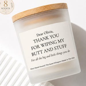 May include: A frosted glass candle jar with a light wood lid and a white label featuring the text: Dear Olivia, THANK YOU FOR WIPING MY BUTT AND STUFF, For all the big and little things you do, 10oz | Hand-Poured | The Sweet Whispers | Made In The USA.