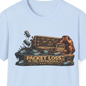 May include: A light blue t-shirt featuring a graphic of a caveman looking at a stone tablet with a network diagram and question marks. The text reads PACKET LOSS IN THE CRETACEOUS, surrounded by small stone blocks labeled PKT scattered on the ground.