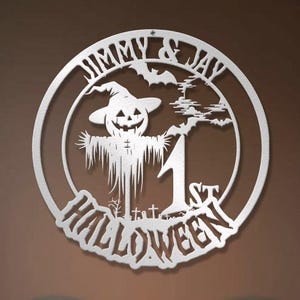 May include: A circular silver metal wall sign featuring a cutout design of a scarecrow with a pumpkin head, bats, and a graveyard. The text reads JIMMY & JAY 1ST HALLOWEEN. The sign is mounted on a wall above a dining table with ghost-themed chairs.