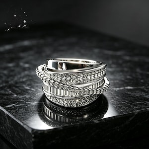 May include: A wide silver-toned ring featuring a multi-layered design with alternating bands of smooth polished metal, a textured rope-like twisted wire, and two rows of small sparkling clear stones set into the metal surface.