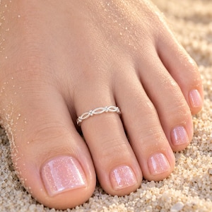 May include: A silver toe ring featuring a repeating open oval and small bead pattern. The band is crafted from polished metal and is worn on the second toe, showcasing a delicate and continuous link design that encircles the toe completely.