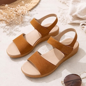 May include: A pair of tan suede-textured sandals featuring a wide front strap, an adjustable ankle strap with a hook-and-loop closure, and a thick, matching tan platform sole with a beige footbed for a neutral and functional footwear design.